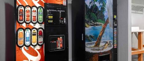 Deux distributeurs automatiques de boissons : l’un arbore le logo Coca-Cola, l’autre représente une plage tropicale.