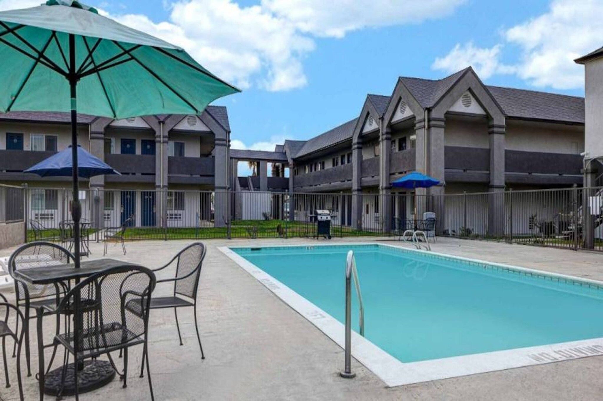 A swimming pool with a patio area, outdoor furniture, and a building with multiple balconies.
