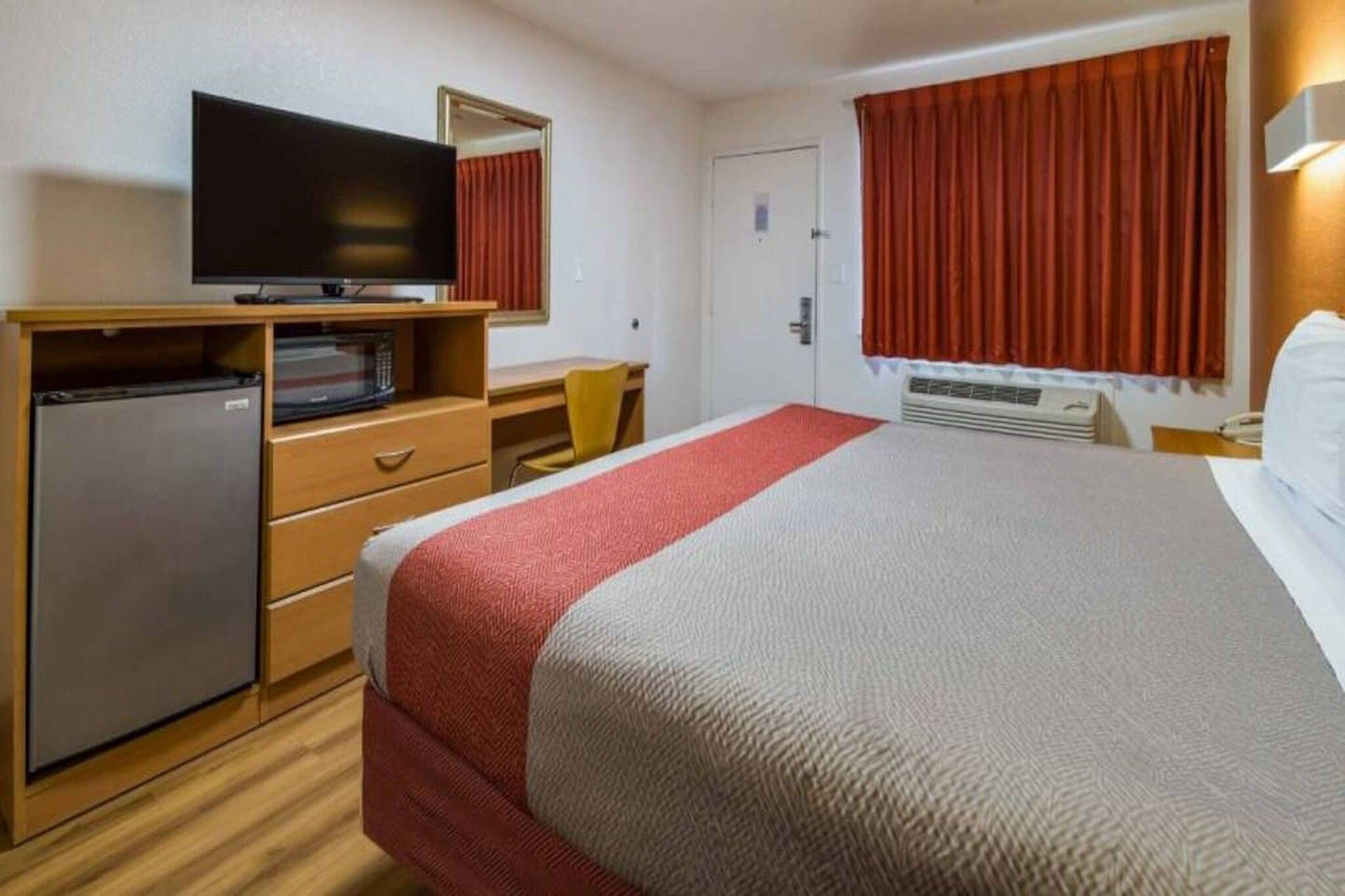 A hotel room with a bed, a television on a wooden dresser, a desk, and a chair.