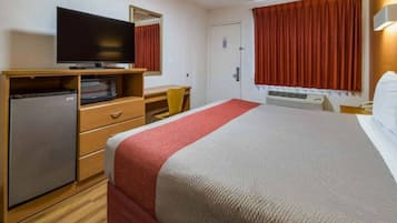 A hotel room with a bed, a television on a wooden dresser, a desk, and a chair.