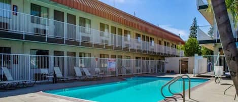 A motel with a swimming pool, a fenced deck area, and a two-story building with balconies.