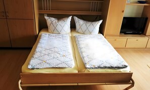 Un lit double avec une couvre-lit à motifs, deux oreillers à pois et un téléviseur posé sur un meuble en bois, à droite.