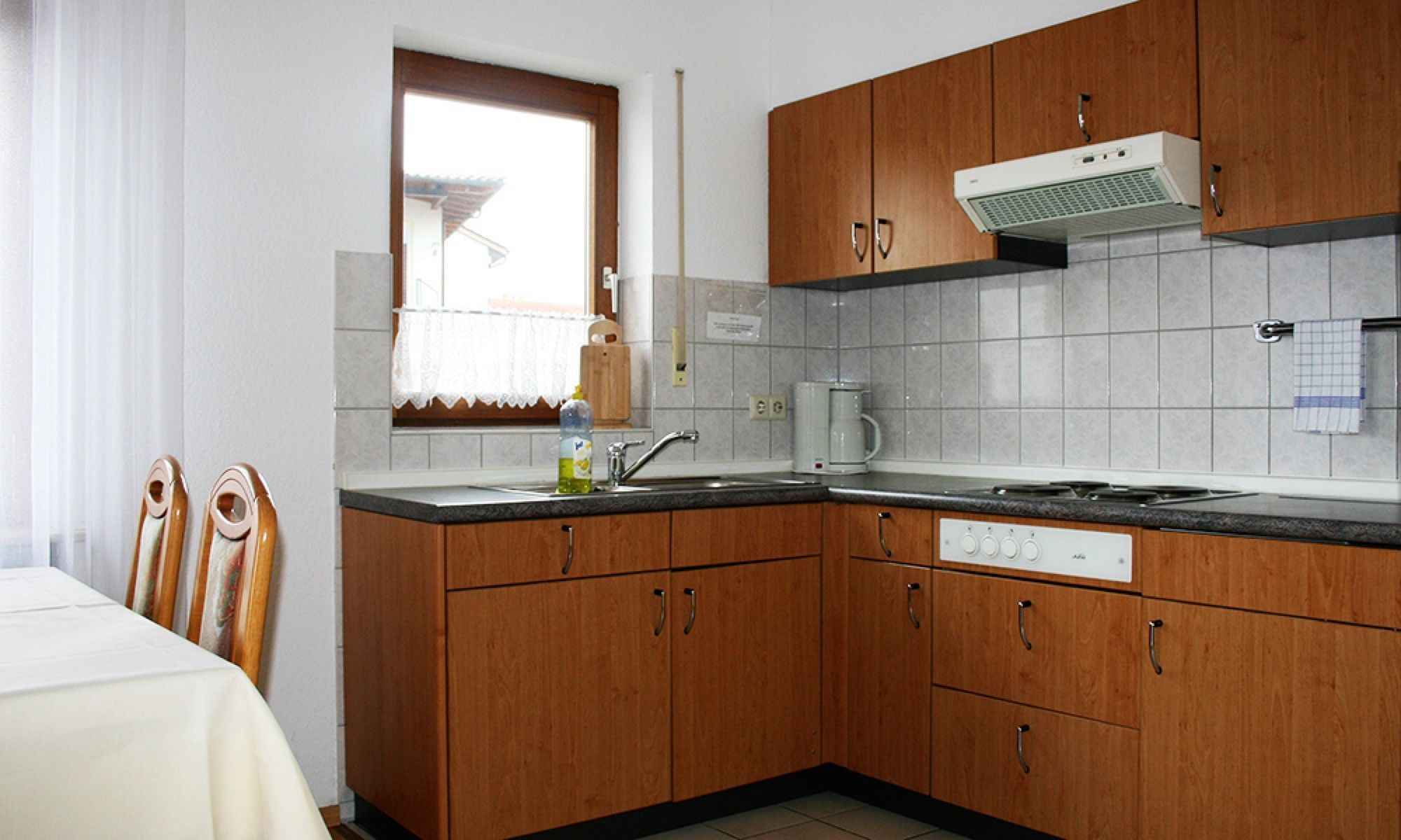 Una cucina con mobili in legno, forno a incasso e finestra con tenda.
