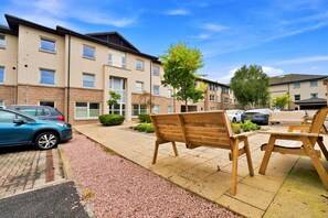 A residential building with multiple windows, a paved walkway, and outdoor seating. - Ness-side Apartment (Inverness)