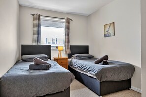 A bedroom with two single beds, a nightstand, a lamp, and a window with curtains. - Ness-side Apartment (Inverness)