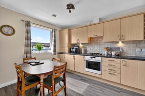 A modern kitchen with wooden cabinets, a gas stove, and a built-in oven. - Ness-side Apartment (Inverness)