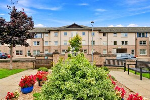 A multi-story building with a flat roof, several windows, and a paved area with benches and potted plants. - Ness-side Apartment (Inverness)