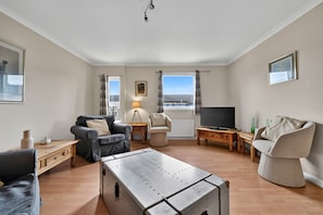 A living room with a sofa, armchair, and a television. - Ness-side Apartment (Inverness)