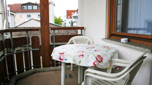 Un balcón con una mesa y dos sillas, una ventana y vistas a edificios.