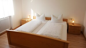 Una cama doble con estructura de madera, dos mesitas de noche con lámparas, un radiador y una ventana con cortinas.