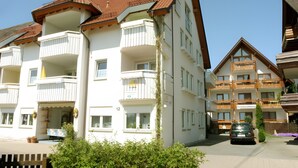 Un hôtel à plusieurs étages doté de balcons, une voiture garée devant et un ciel dégagé.