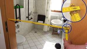 Une salle de bain équipée de toilettes, d’un lavabo, d’une douche et d’un mètre ruban indiquant la hauteur de la pomme de douche.