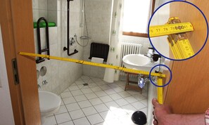 Un baño con inodoro, lavamanos, ducha y un metro que marca la altura del cabezal de la ducha.