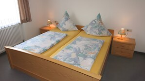 Un lit double avec une literie à motifs floraux, deux tables de chevet avec des lampes, un radiateur et une fenêtre avec des rideaux.