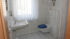 Une salle de bain avec un lavabo, des toilettes et une douche, le tout de couleur blanche.