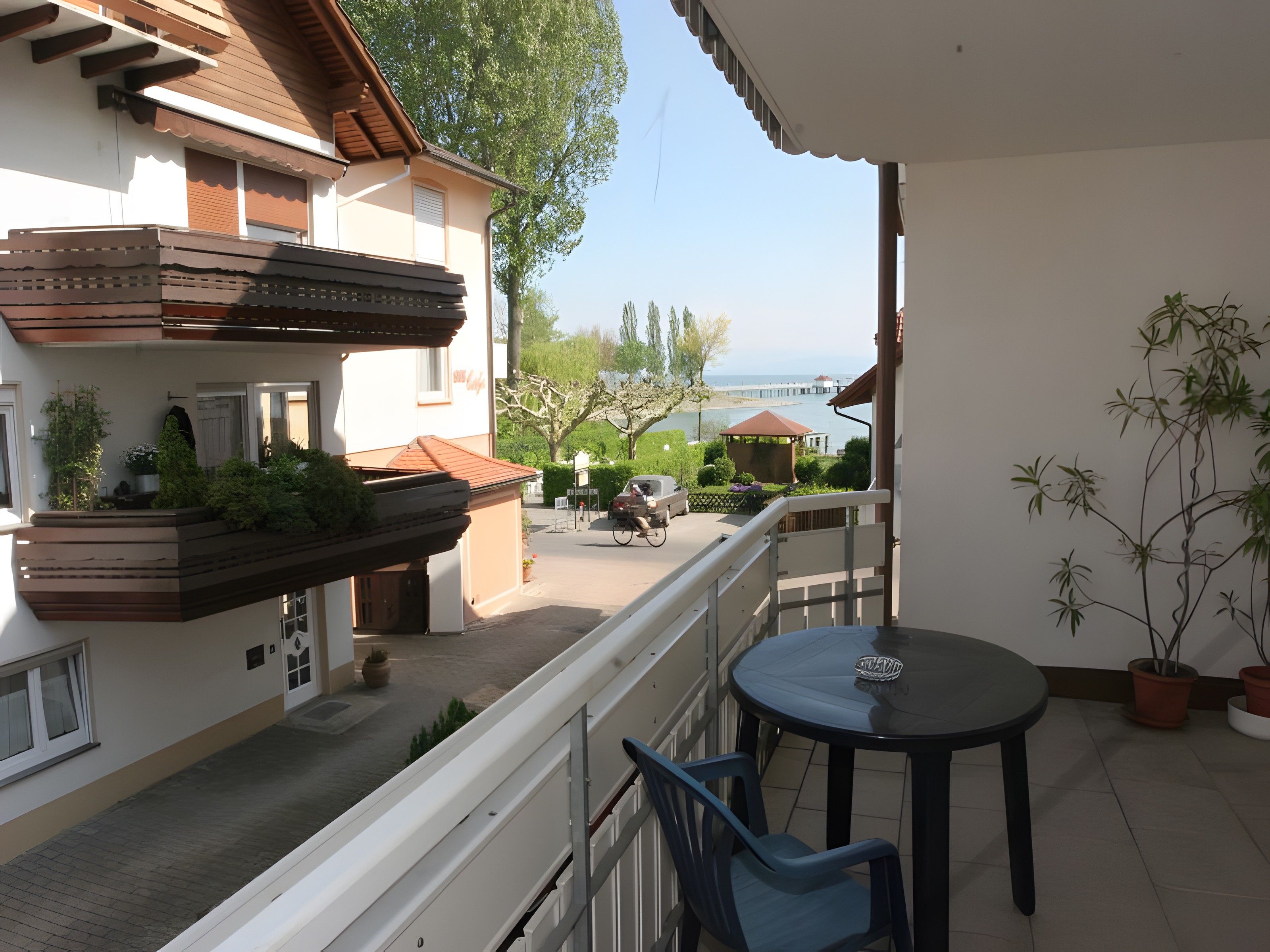 Ein Balkon mit Tisch und Stühlen, mit Blick auf eine Straße, ein Gebäude und den See.