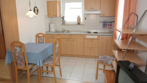 Une cuisine compacte avec des meubles en bois, une table à manger avec des chaises, un four encastré et un téléviseur.