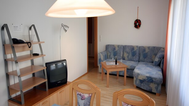 Uma sala de estar mobiliada com sofá, televisão, mesa e abajur.