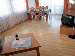 Ein Wohnzimmer mit Essbereich, Holzböden, einem Fernseher und einem Tisch mit einer Flasche und Gläsern.