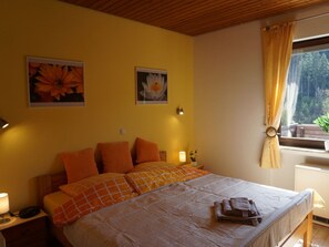 Ein Schlafzimmer mit Bett, Kissen, einem Nachttisch, einer Lampe und einem Fenster mit Vorhängen.