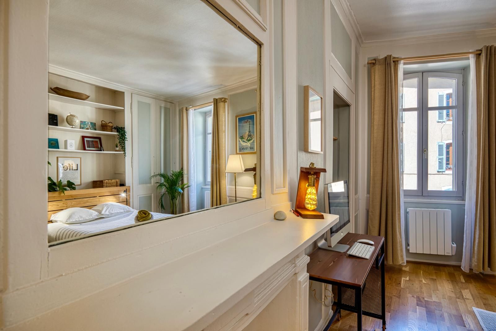 A hotel room with a bed, bedside table, lamp, and a large mirror reflecting the room.