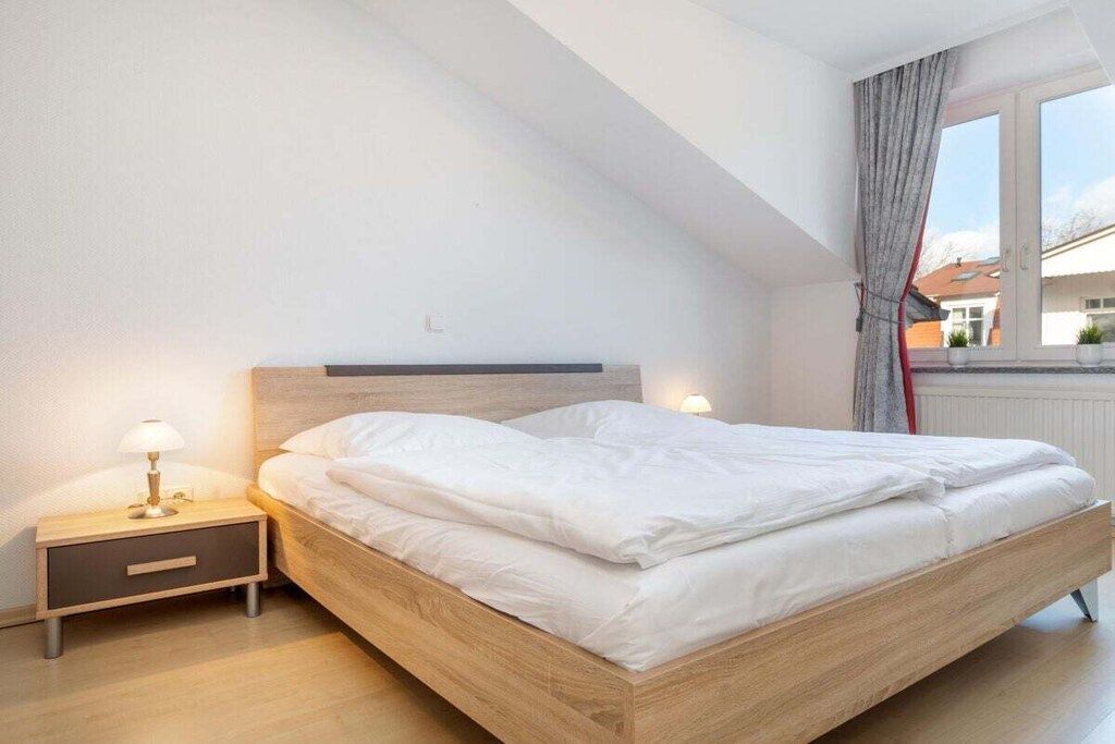 Quarto com cama de madeira, mesa de cabeceira com abajur e janela com cortinas.