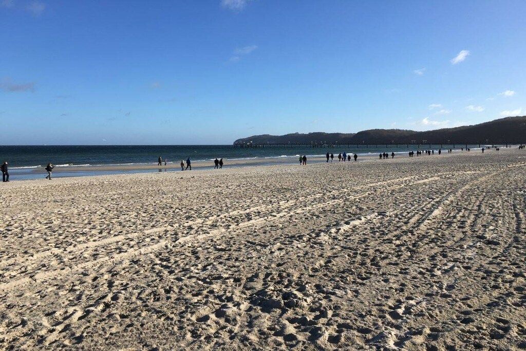 Ein weiter Sandstrand mit Fußspuren, ein klarer Himmel und ein Pier in der Ferne.