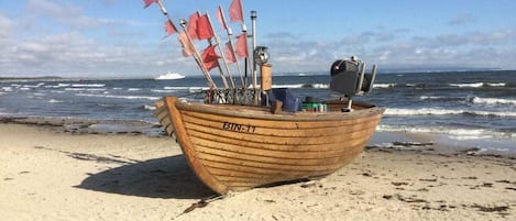 A wooden boat with the number BIN-11 on a sandy beach with the ocean in the background.