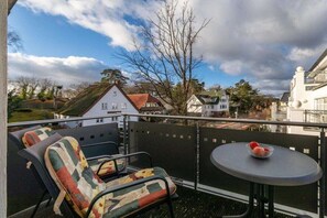 Een balkon met een tafel en twee stoelen, een uitzicht op huizen en een bladerloze boom.