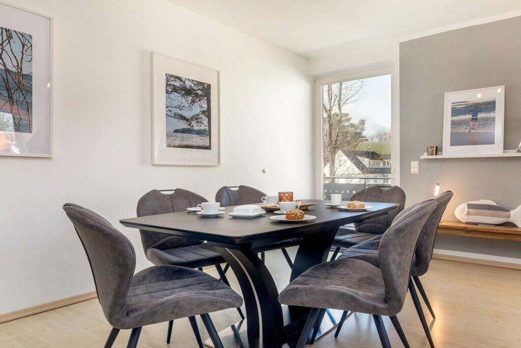 A dining area with a round table, grey upholstered chairs, and framed artwork on the walls.