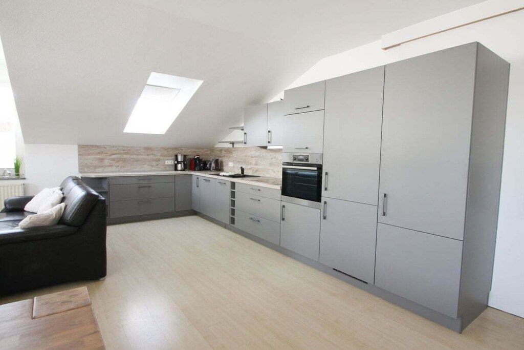 A modern kitchen with grey cabinets, a built-in oven, and a skylight.