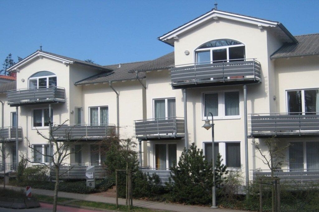 A row of modern residential buildings with balconies, a clear sky, and a street sign indicating the number 6.