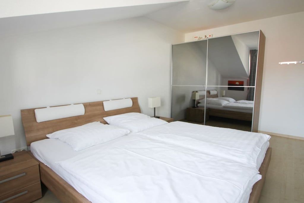 A single bed with a wooden headboard, a bedside table with drawers, and a mirror cabinet on the wall.