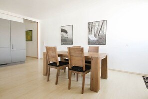A dining area with a wooden table and chairs, a white wall with two framed pictures, and a light-colored floor. - Holiday apartment with 1 bedroom (Ostseebad Binz)