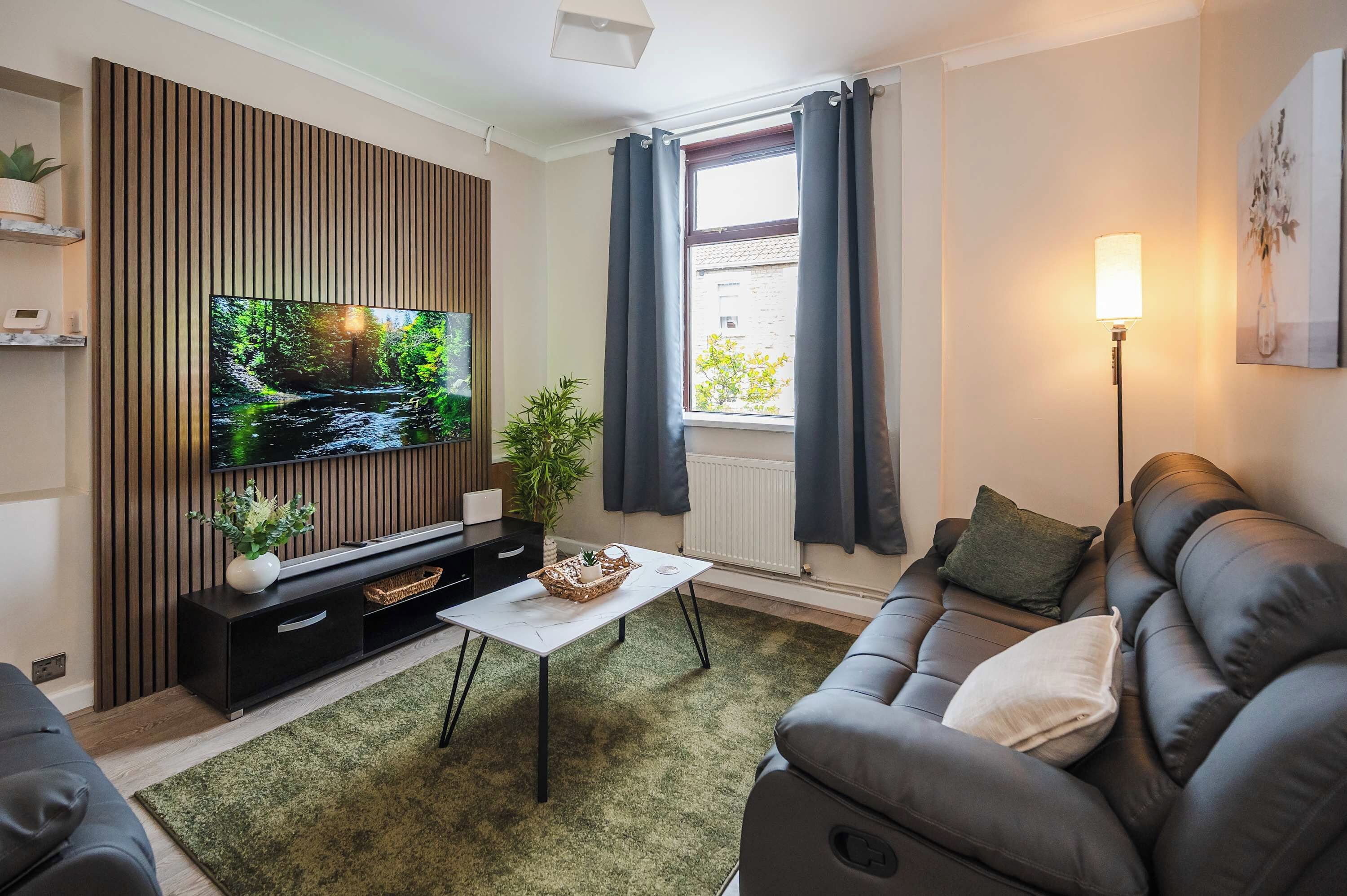 A modern living room with a flat-screen TV, a sofa, a coffee table, and a potted plant.