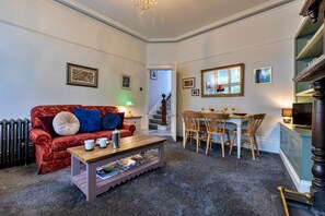 A living room with a red sofa, a coffee table, and a dining area with wooden chairs and a table. - Hall Bank (Buxton)