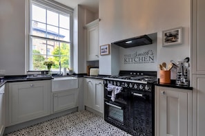 A kitchen with a black and white patterned floor, a black stove, and a window with a view of buildings and greenery. - Hall Bank (Buxton)