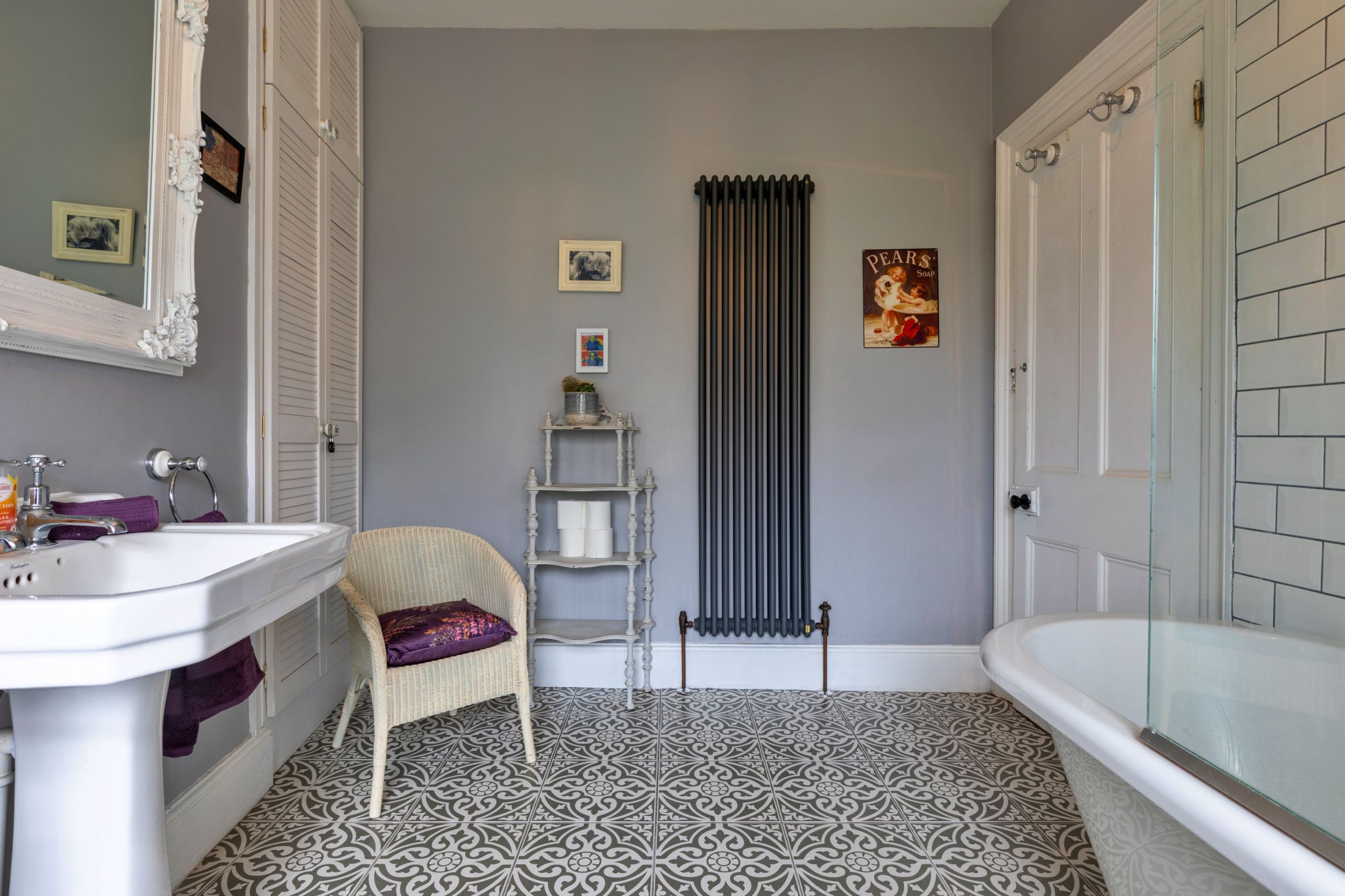 Une salle de bain avec un lavabo blanc, une baignoire, un radiateur et des carreaux de sol à motifs.