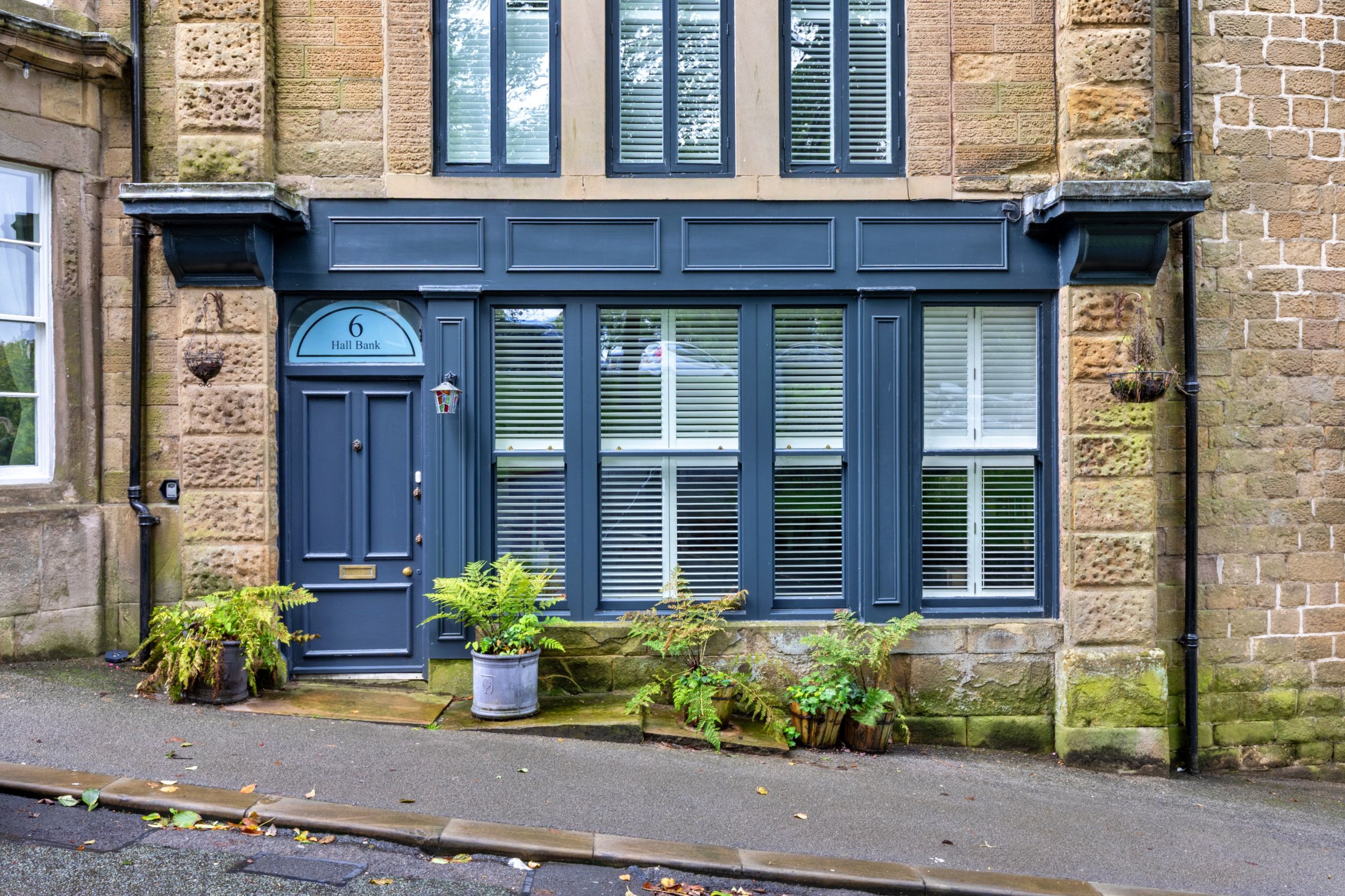 A traditional stone building with a dark blue door, multiple windows with shutters, and a small porch area with potted plants.