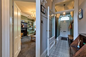 A hallway with a carpeted floor, a door with a sign, a chandelier, and a patterned tile floor. - Finest Retreats | Hall Bank (Buxton)