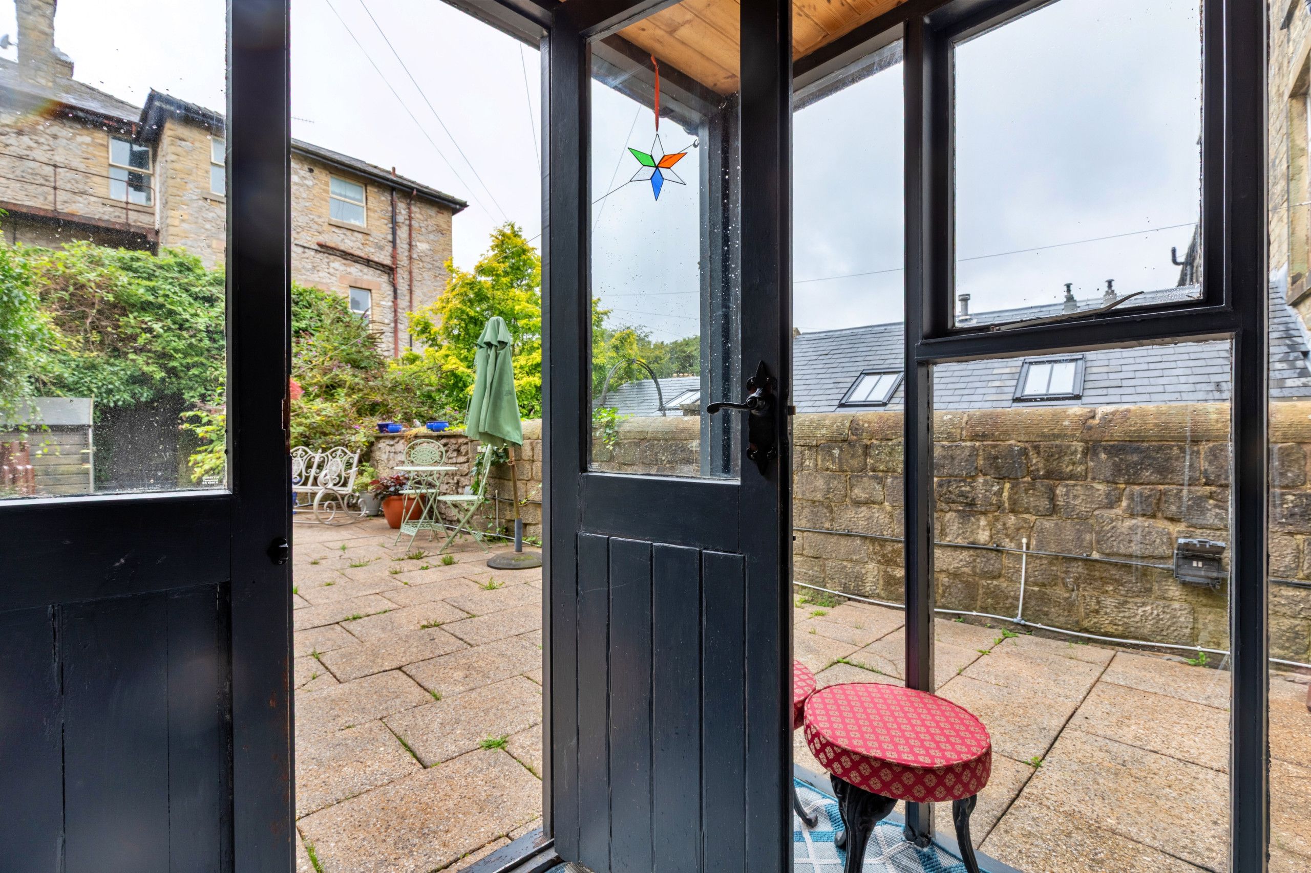 A glass door leading to a patio with a small round table and chairs, a green umbrella, and a stone wall.