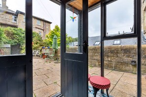 A glass door leading to a patio with a small round table and chairs, a green umbrella, and a stone wall. - Hall Bank (Buxton)