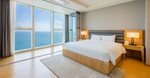 A modern hotel room with a large bed, two bedside tables with lamps, a view of the sea, and a large window. - LCT Residence the Drayton (Busan)
