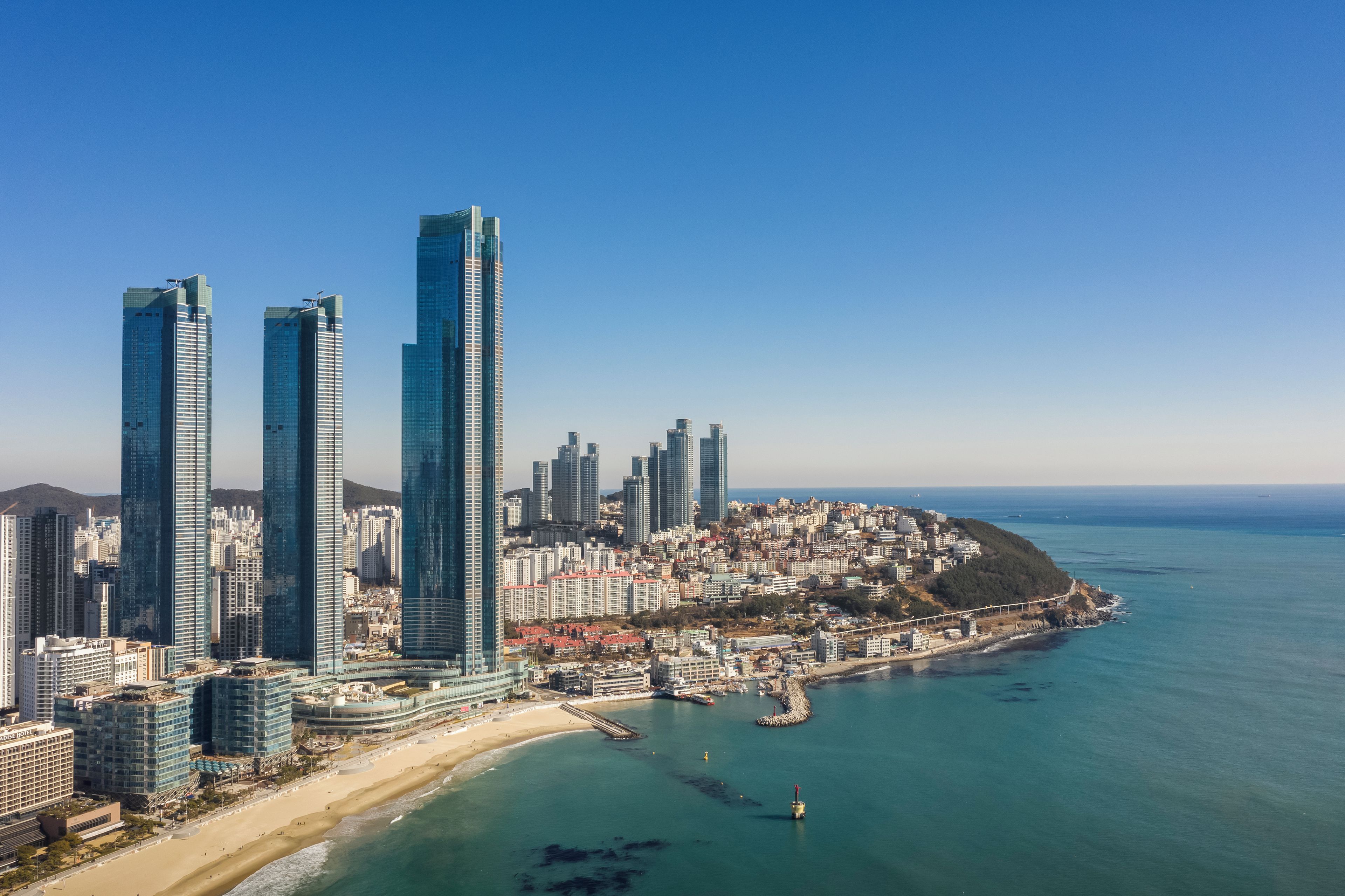A coastal cityscape with high-rise buildings, a beach, and a pier.