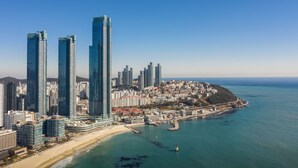 Un paisaje urbano costero con rascacielos, una playa y un muelle.