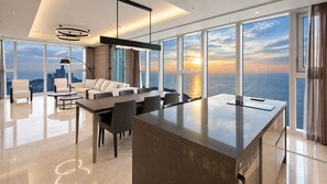 A modern interior with a dining area, sofas, and a large window offering a view of the sea and cityscape. - LCT Residence the Drayton (Busan)