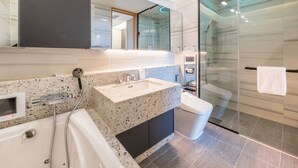 Un baño moderno con una bañera independiente, un lavabo con encimera de granito, una ducha con mampara de cristal y un inodoro.