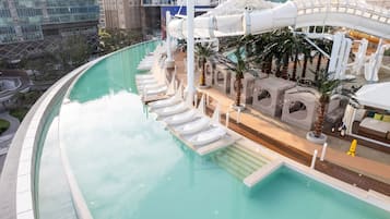 A pool area with a water slide, lounge chairs, and palm trees.