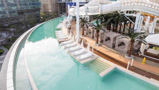 Zona de piscina con tobogán de agua, sillas de descanso y palmeras.