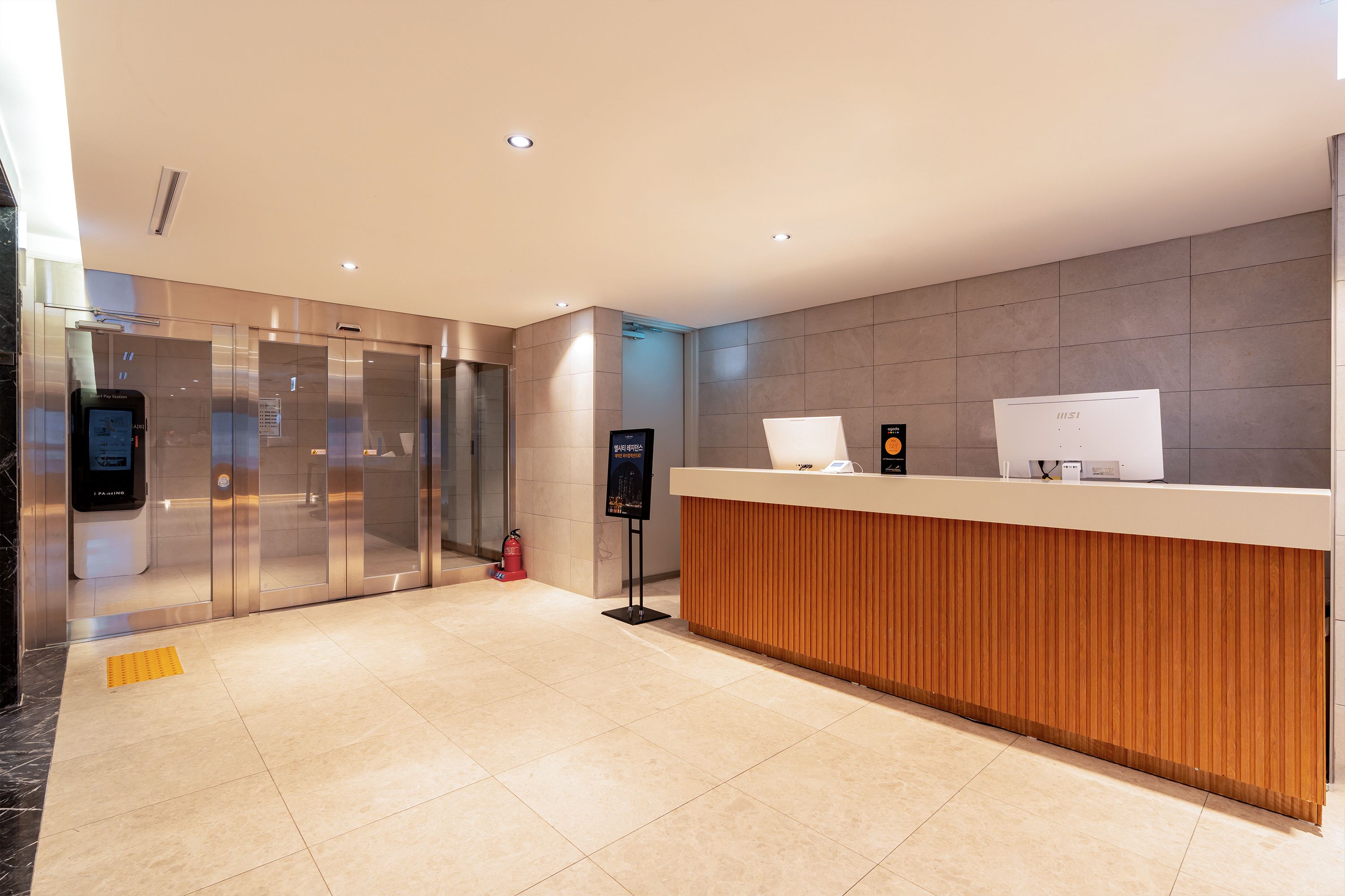 A modern reception area with a wooden reception desk, glass elevator doors, and a digital information kiosk.
